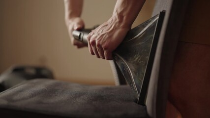 Close-up view of housewife using professional vacuum cleaner with upholstery nozzle, removing dirt and dust from fabric-covered chair for thorough hygiene at home. Concept of household cleanliness.