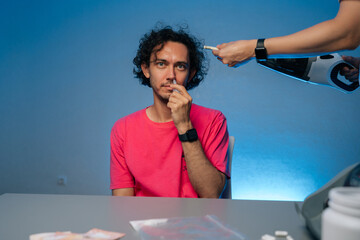 Man looking at camera sitting at table receiving bizarre hair vacuum treatment while applying nasal...
