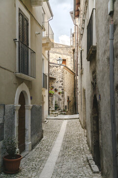 View of narrow cobblestone street lined with aged buildings exhibiting a mix of light and shadow, leading the eye deeper into the heart of the village, Pacentro, Abruzzo, Italy.