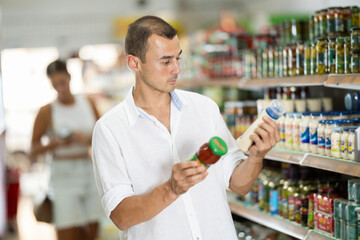 Man near department display of spicy in hypermarket. Buyer chooses between variation of sauce, considers various options sauce, compare items