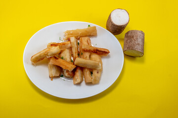 Cassava Fries on Plate with Fresh Cassava Root over Yellow Background