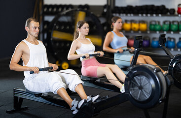 Young athletic man in sportswear training on rowing machine in gym..