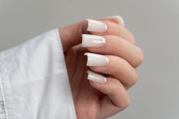 Long white nails – glossy manicure on female hand in white shirt, professional nail care. The person is wearing a white shirt, adding an elegant contrast to the manicured nails. 