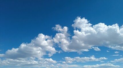 A vibrant blue sky showcases a collection of soft, white clouds drifting lazily, creating a peaceful atmosphere in the afternoon light.