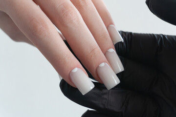 White ombre manicure – close-up of hands in black glove, professional nail art salon style. The nails are well-shaped with a glossy finish, reflecting careful and precise nail art.