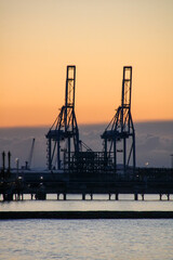 Obraz premium Sunrise at Platja de la Pineda, Vila-seca, Tarragona, Catalonia, Spain, with views of the port and Tarragona’s cargo cranes over the Mediterranean Sea.