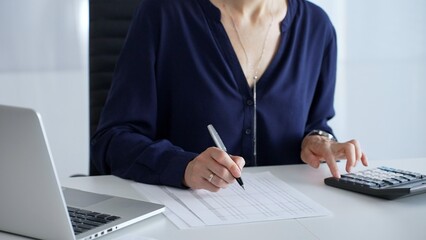 Professional female accountant analyzing financial documents, using magnifying glass and calculator at workplace desk, focused on detailed accounting review, close up. Audit and taxes in business