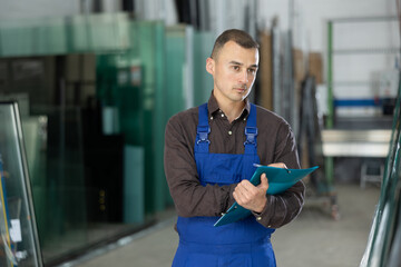 Skilled technician in blue overalls carefully inspecting glass panels, focused on quality check,...