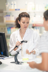 Obraz premium Adult female pharmacist in uniform punches medicines at checkout counter in pharmacy