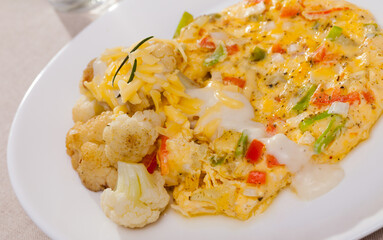 Delicious vegetable omelette served on white plate with cauliflowers, grated cheese and cream sauce..