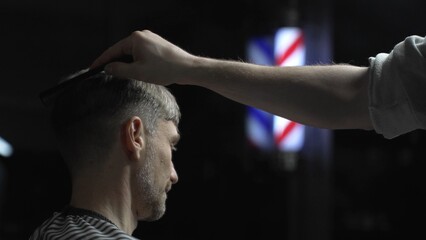 Professional barber carefully checking customer's hair texture and head contours, preparing for precise haircut, vintage barbershop interior with iconic striped pole visible