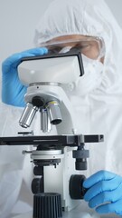 Male virologist in a hazmat suit, mask, and blue gloves, diligently working at a microscope in a laboratory researching viruses. Medicine, science concept