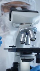 Medical virologist in a hazmat suit, mask, and gloves, diligently working at a microscope in a laboratory researching viruses. Healthcare and science concept