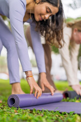 Young women rolling yoga mat after exercising in urban park
