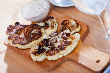 Delicious vegetarian dish of grilled cauliflower served with spicy white sauce on wooden board..