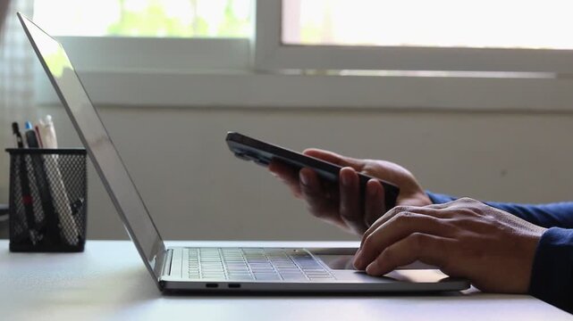 Businessman using laptop and mobile phone to enter password for two-factor authentication. Cybersecurity, privacy protection, secure login, identity verification, and online banking or digital payment