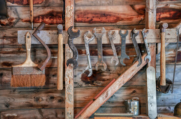 Vintage rustic hand tools hanging on wooden workshop wall for carpentry and repair