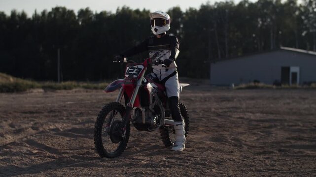 Moto crosser in protective suit and helmet sits on motorcycle