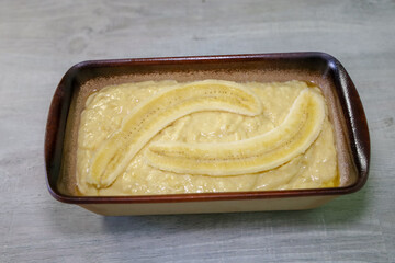 Banana bread batter in a stoneware loaf pan with fresh banana on top.