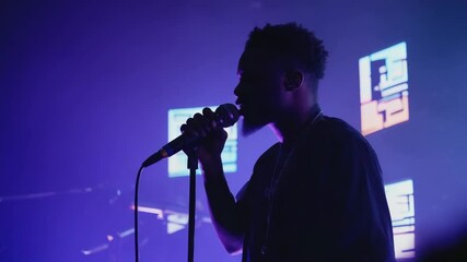 Male singer captivating audience with powerful vocals during live performance on stage, illuminated by vibrant and colorful lighting effects, creating an electrifying atmosphere