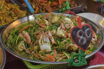 A large metal platter with a mouth-watering dish of crabs fried with vegetables and herbs in a fragrant sauce.  