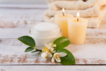Close-up of orange blossoms with a container of cream, next to a pair of candles and towels in the background.
