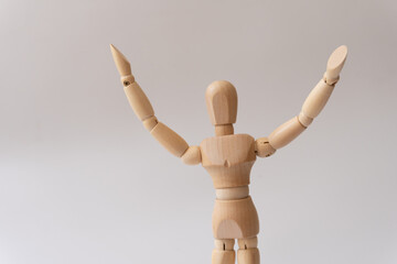 Close-up of a wooden mannequin with arms raised, expression of joy