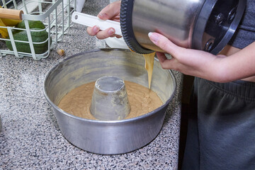 On a marble table, cake batter is being poured into a metal container to be baked.