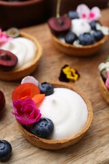 Sweet tartlets with berries and flowers on wooden board, closeup. Delicious dessert