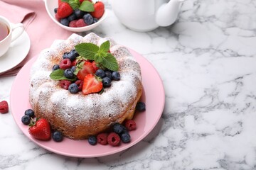 Tasty Bundt cake with powdered sugar and berries on white marble table, space for text