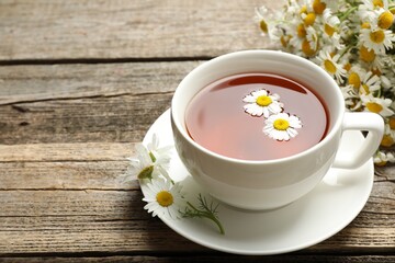 Aromatic tea in cup and chamomile flowers on wooden table, closeup