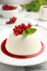Delicious panna cotta with red currants, sauce and mint on white marble table, closeup