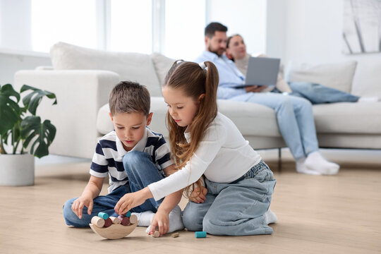 Children feeling comfortable on warm floor, while their parents sitting on sofa at home. Underfloor heating