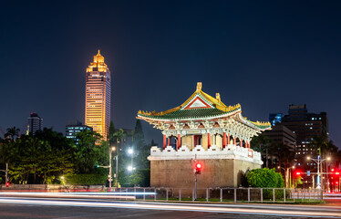 Fototapeta premium The historic Jingfu Gate (East Gate) in a traffic circle at night, with Taipei modern city skyline and traffic light trails in the background, Taiwan