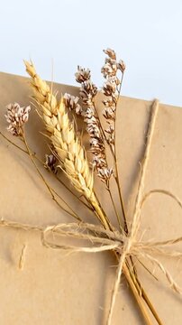 Brown Paper Wrapped Gift with Dried Flowers and Twine Tie on White Surface against Green Garden Backdrop in Bright Daylight