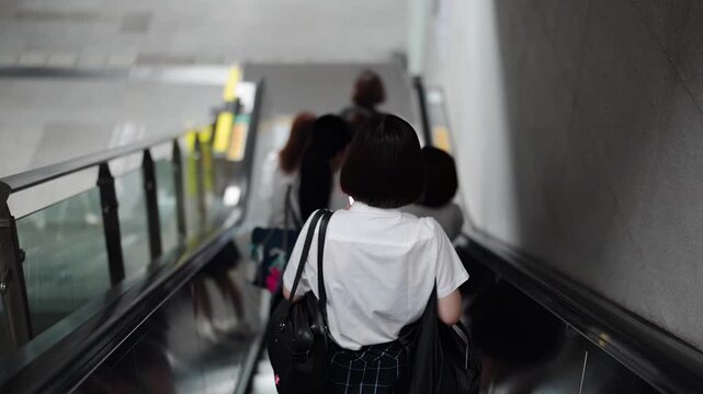 Slow-motion. Japanese high school girls in uniform descend an escalator while using smartphones, chatting and adjusting bags as steps glide below too. Shanghai's Pudong New District. China. Spring.