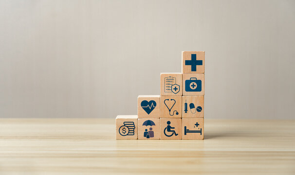 Healthcare planning and medical insurance concept with hand arranging wooden blocks showing icons of stethoscope, finance, first aid, heart health, and cross symbol on blue background