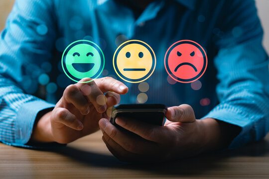 Customer satisfaction feedback concept showing person using mobile phone to select emotion face rating with happy, neutral, sad smiley icons representing service review and user experience evaluation