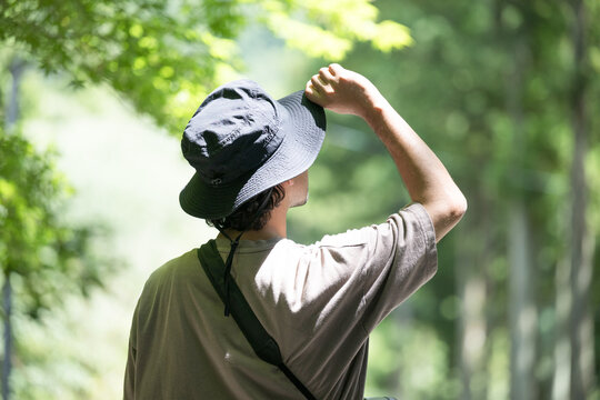 森やキャンプ、アウトドアや登山で緑を眺める帽子を被った男性の後ろ姿顔無し