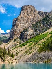 Towering rocky mountain cliff with green slopes above turquoise Moraine lake