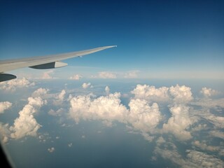 A stunning natural landscape. White clouds can be seen flying across the clear blue sky through the window under the plane's wing.
