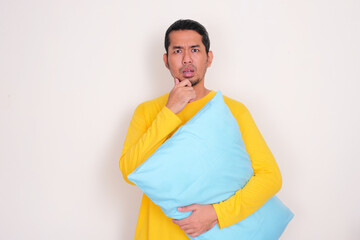 Adult Asian man holding a pillow showing confused face expression