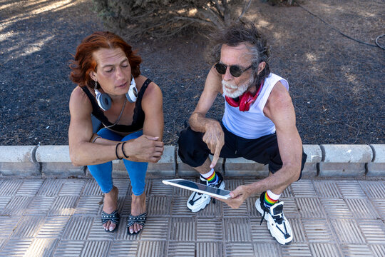 Transgender person and friend using tablet and wearing headphones in a park - Powered by Adobe