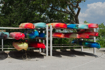 Colorful Rental Kayaks Arranged on a Rack by an Outdoor Nature Setting. Brightly colored kayaks are...