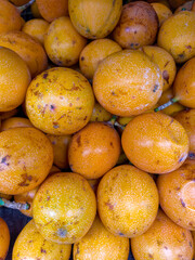 Close-up of ripe yellow-orange granadillas with speckled skin, stacked together at a market, showcasing their tropical freshness.