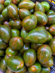 A bunch of green tomatoes are piled up in a basket. The tomatoes are of different sizes and are arranged in a way that they are not touching each other. The basket is placed on a table