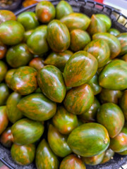 A bunch of green tomatoes are piled up in a basket. The tomatoes are of different sizes and are arranged in a way that they are not touching each other. The basket is placed on a table