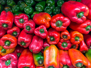 A bunch of red and green peppers are piled on top of each other. The peppers are fresh and ready to be eaten