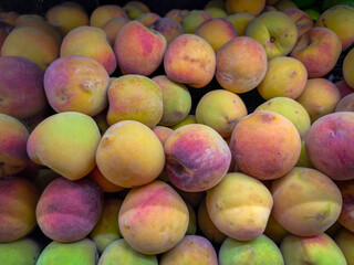 Close-up of fresh peaches with soft skin in shades of yellow, orange, and red, stacked at a market, highlighting their natural texture and ripeness.