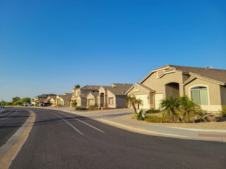 Obraz premium Arizona residential neighborhood with typical single family houses along curving street with xeriscaped roadside under clear blue sky in summer